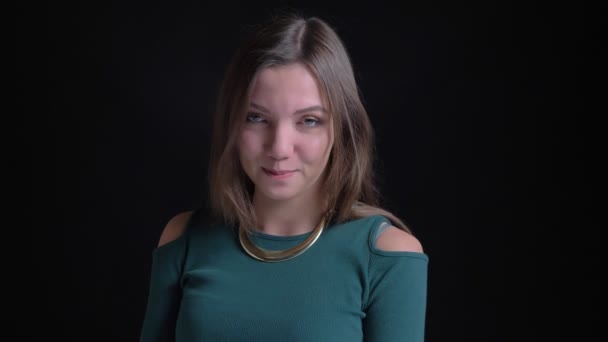Porträt eines jungen brünetten kaukasischen Mädchens, das schüchtern lacht und auf schwarzem Hintergrund in die Kamera schaut. — Stockvideo
