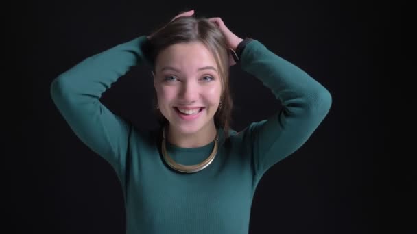 Porträt einer jungen brünetten Kaukasierin, die in die Kamera lächelt und auf schwarzem Hintergrund kokett ihr Haar schüttelt. — Stockvideo