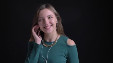 Yakın çekim kulaklık müzik dinleme ve sevinçle dans siyah arka plan üzerine genç esmer beyaz kız portresi.