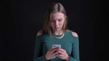 Genç esmer beyaz kız smartphone siyah arka plan üzerine ciddi içine izlerken portresi