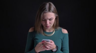 Genç esmer beyaz kız smartphone ile siyah arka plan üzerinde şaşkınlık içine izlerken portresi.