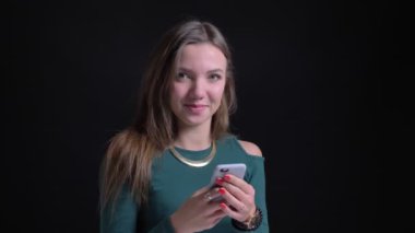 Smartphone ile çalışma ve sevinçle kamera siyah arka plan üzerine içine izlerken genç esmer beyaz kız portresi.
