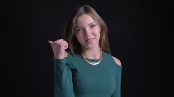 Retrato de jovem morena caucasiana menina gestando sinal de dedo para cima para mostrar como e respeito no fundo preto . — Vídeo de Stock