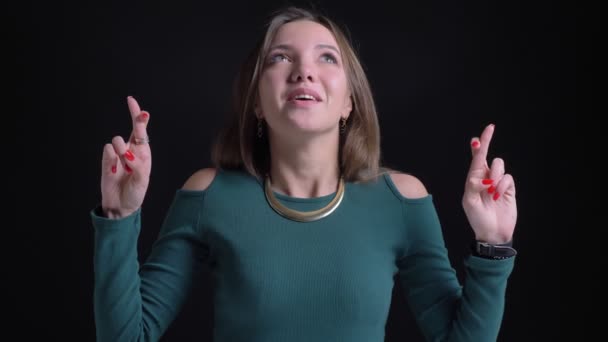 Retrato de una joven morena caucásica haciendo gestos de dedos cruzados para mostrar esperanza sobre fondo negro . — Vídeos de Stock