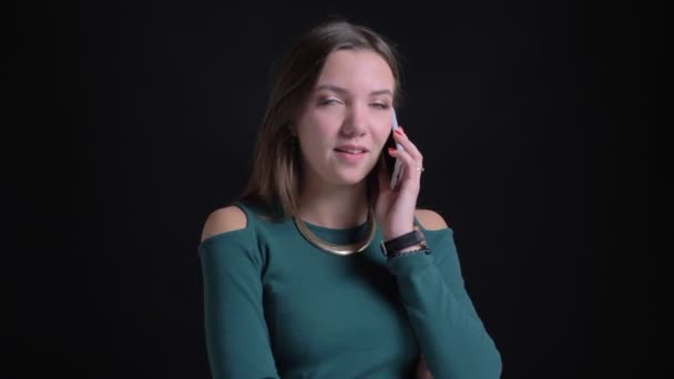Porträt eines jungen brünetten kaukasischen Mädchens, das auf seinem Smartphone freudig auf schwarzem Hintergrund spricht. — Stockvideo