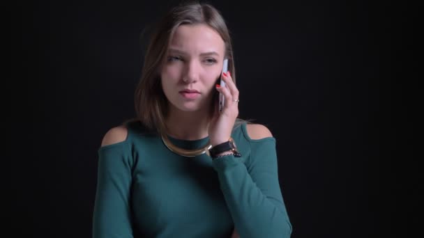 Porträtt av ung brunett kaukasiska flicka talar på smartphone med glädje och justera hår på svart bakgrund. — Stockvideo