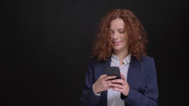 Primer plano retrato de mujer caucásica adulta escribiendo en el teléfono mirando a la cámara y lanzando su pelo rizado rojo — Vídeos de Stock