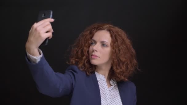 Closeup portret van volwassen Kaukasische mooie vrouw met rode krullend haar nemen van selfies op de telefoon voor de camera — Stockvideo