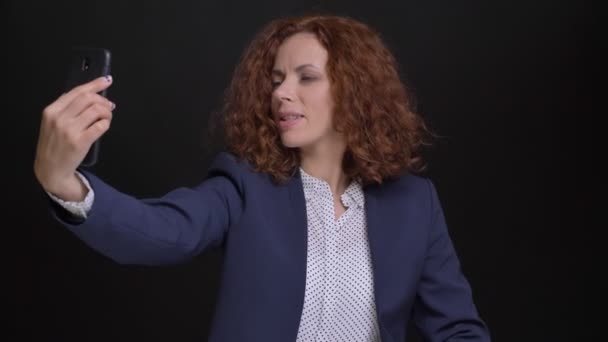 Nahaufnahme Porträt einer erwachsenen kaukasischen attraktiven Frau mit roten lockigen Haaren, die einen Videoanruf am Telefon hat und fröhlich winkt Tschüss — Stockvideo