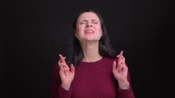 Closeup portrait of adult pretty caucasian woman having her fingers crossed anxiously and praying hopefuly in front of the camera — Stock Video