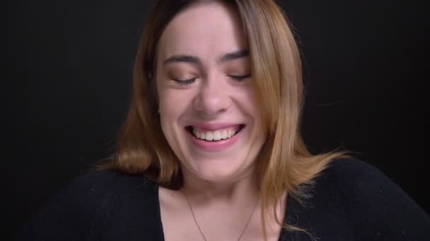 Closeup portret van jonge vrolijke Kaukasische vrouwelijke glimlachen en lachen gelukkig, terwijl het zoeken van st camera met geïsoleerd op zwarte achtergrond — Stockvideo
