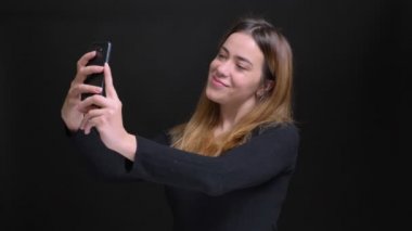 Siyah arka plan ile kamera önünde poz telefon üzerinde selfies alarak genç beyaz kadın portresi closeup izole