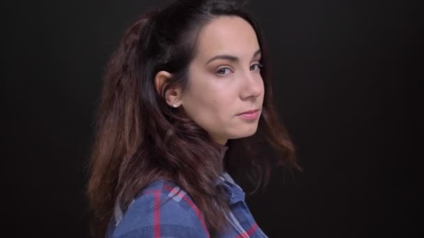 Närbild porträtt av unga vackra kaukasiska kvinnliga svarvning från sida och tittar på kameran med bakgrunden isolerade på svart — Stockvideo
