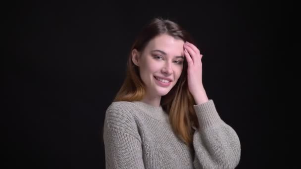 Closeup retrato de jovem caucasiana sedutora fêmea sorrindo fixando seu cabelo e posando na frente da câmera com fundo isolado em preto — Vídeo de Stock