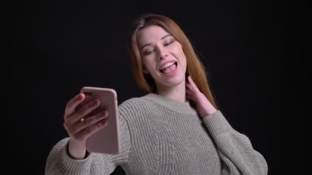 Primer plano retrato de joven hermosa chica caucásica tomando selfies en el teléfono posando delante de la cámara — Vídeo de stock