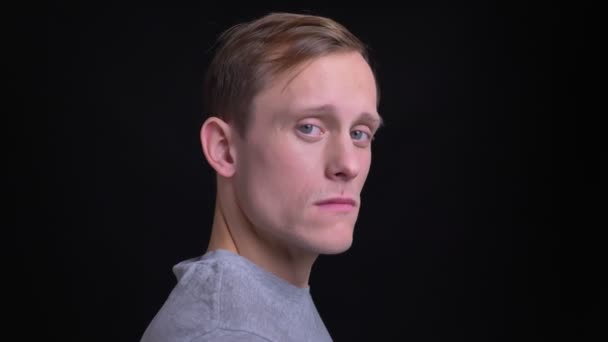 Gros plan vue de côté portrait de jeune homme caucasien attrayant tournant la tête à la caméra et regardant vers l'avant avec fond isolé sur noir — Video