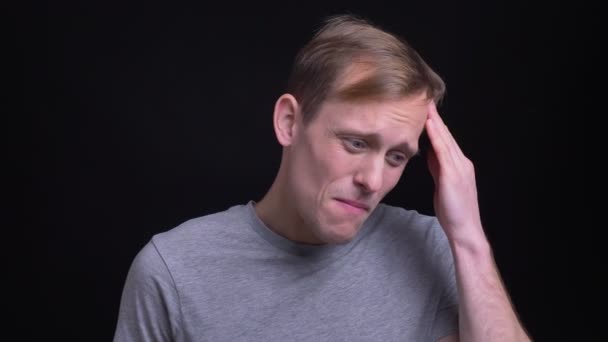 Closeup portrait of young attractive caucasian man getting a headache in front of the camera with background isolated on black — Stock Video