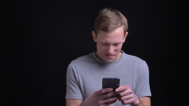Крупним планом портрет молодого привабливого кавказького чоловіка смс по телефону, а потім дивиться прямо на камеру — стокове відео