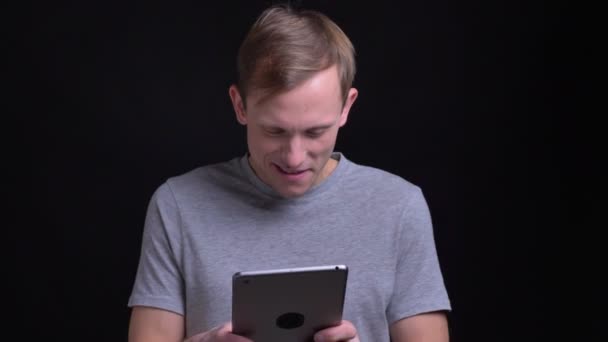 Primer plano retrato de joven atractivo hombre caucásico usando la tableta riendo mirando a la cámara y sonriendo felizmente — Vídeos de Stock