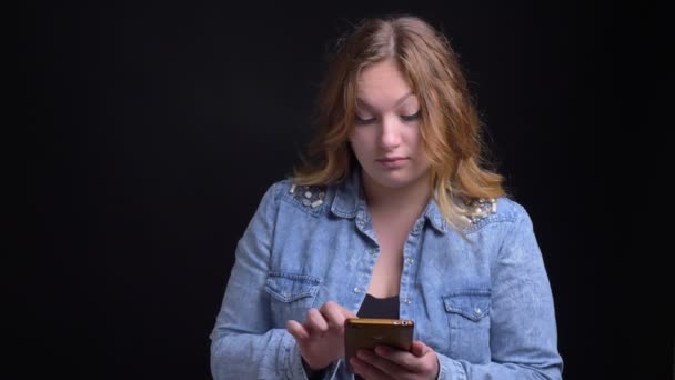 Gros plan portrait d'adulte caucasien femelle textos au téléphone avec sourire excitable avec fond isolé sur noir — Video