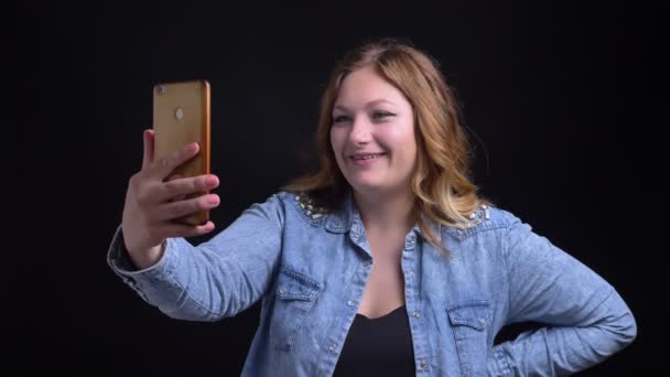 Крупним планом портрет дорослої білошкірої жінки з коротким волоссям, що має відеодзвінок по телефону посміхаючись і випадково махаючи привіт — стокове відео