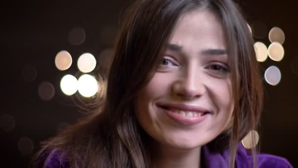 Retrato de close-up de jovem atraente mulher caucasiana sorrindo e sonhando enquanto olha para a câmera com luzes noturnas no fundo — Vídeo de Stock