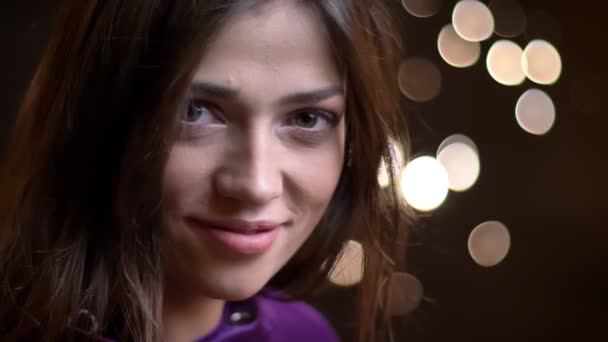 Closeup portrait of young seductive caucasian female smiling and looking straight at camera with night lights on the background — Stock Video