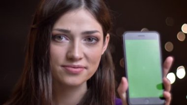 Bir telefon tutarak ve yeşil ekran kamera gülümseyen için gösterilen genç güzel beyaz kadın portresi portre