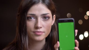 Bir telefon tutarak ve yeşil renk tuşlu ekran kamera için gösterilen ve gülümseyen genç oldukça beyaz kadın portresi portre