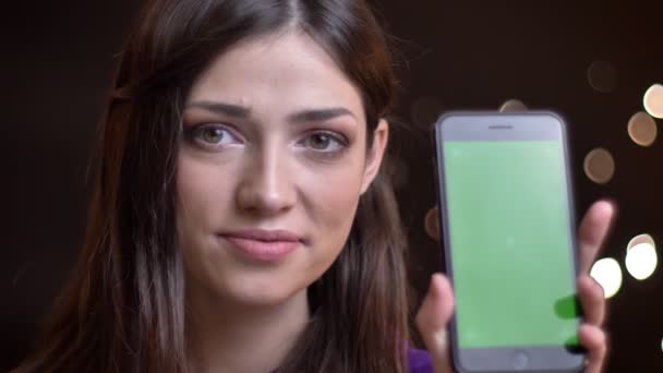 Gros plan portrait de jeune belle femme caucasienne tenant un téléphone et montrant écran vert à la caméra souriant — Video