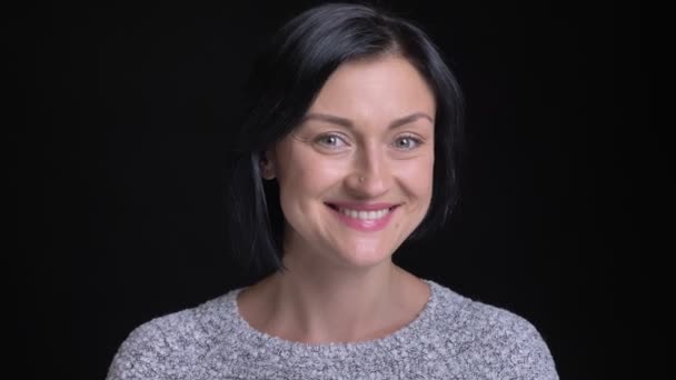 Closeup portrait of young beautiful caucasian woman with short black hair being cute and smiling while looking straight at camera — Stock Video