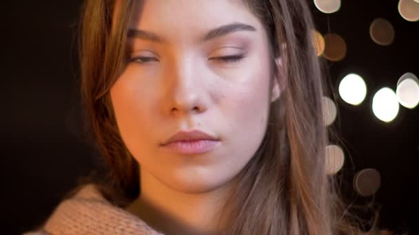 Gros plan portrait de jeune fille caucasienne regardant sérieusement dans la caméra sur fond de lumières floues . — Video