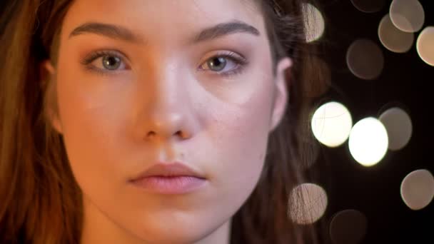 Крупним планом портрет молодої кавказької дівчини, яка спокійно дивиться в камеру на розмитому фоні світла . — стокове відео