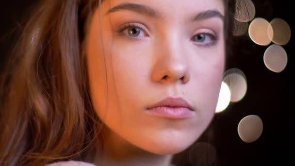 Gros plan portrait en profil de jeune fille caucasienne regarder calmement dans la caméra sur fond de lumières floues . — Video