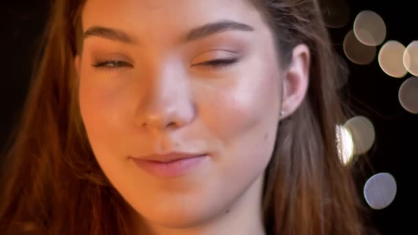 Close-up ritratto di giovane ragazza caucasica annuisce approvando nella fotocamera su sfondo luci sfocate . — Video Stock