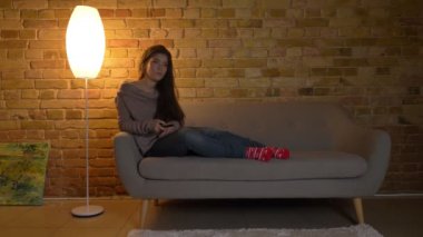 Kanepede oturan ve kanalları Tv de rahat ev arka plan üzerinde anahtarlama genç ve güzel beyaz kız portresi.