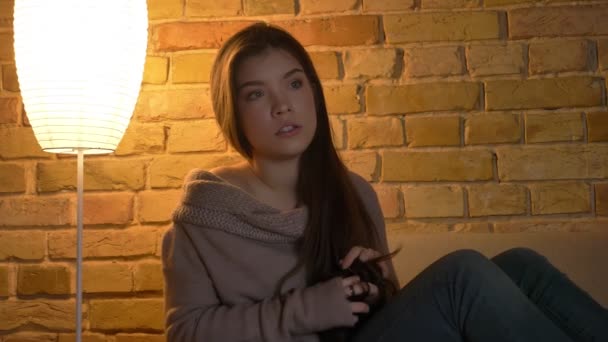 Detailní portrét mladé a krásné kavkazský dívky sedí na pohovce a sledování televize nervózně v útulném domácím prostředí. — Stock video