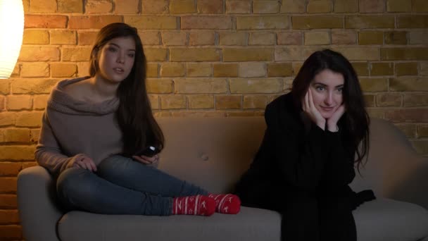 Макро портрет молодих дівчат кавказька, сидячи на дивані і дивитися телевізор уважно на затишному фоні будинку. — стокове відео