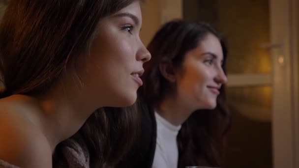 Портрет крупным планом в профиль молодых кавказских девушек, внимательно смотрящих телевизор на уютном домашнем фоне . — стоковое видео