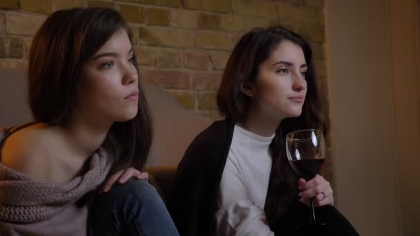 Gros plan portrait en profil de jeunes filles caucasiennes regardant la télévision attentivement et buvant du vin sur fond de maison confortable . — Video