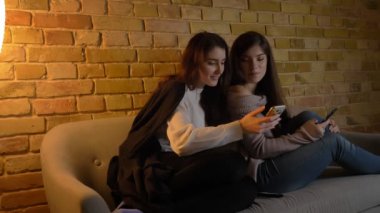 Kanepede oturan ve rahat ev atmosferde sevinçle kendi smartphones içine izlerken genç beyaz kız portresi.