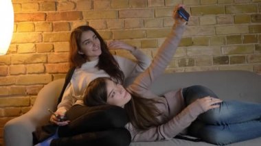 Kanepede rahatlatıcı ve selfie-fotoğrafları yapma genç beyaz kız portre rahat ev atmosferde smartphone kullanarak.