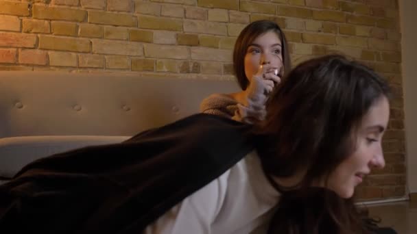 Портрет веселых молодых кавказских девушек, сидящих на полу, пьющих вино и смотрящих фильм в уютной домашней обстановке . — стоковое видео