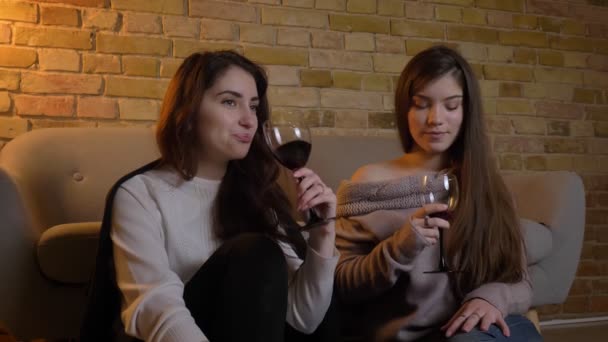 Portrait de jeunes filles caucasiennes joyeuses assises sur le sol buvant du vin et communiquant dans une atmosphère chaleureuse à la maison . — Video