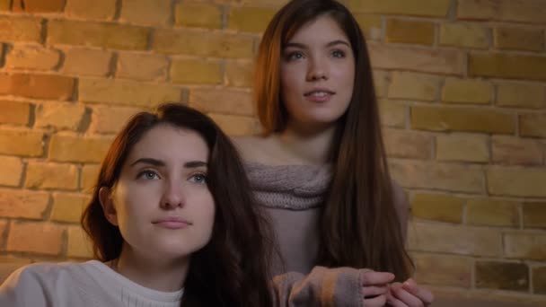 Retrato de chicas caucásicas jóvenes sentadas juntas y viendo películas con atención en un acogedor ambiente hogareño . — Vídeos de Stock