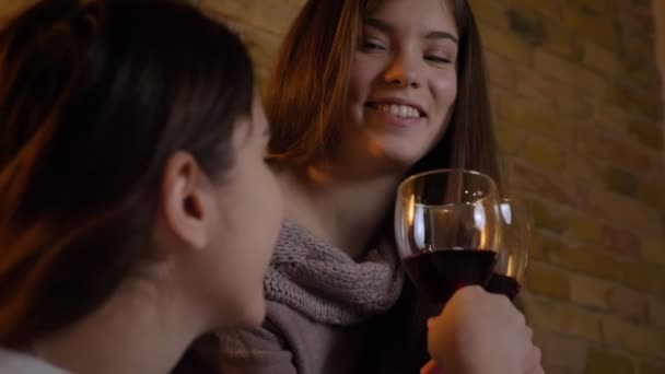 Gros plan portrait de jeunes filles caucasiennes joyeuses assises ensemble et buvant du vin dans une atmosphère chaleureuse à la maison . — Video