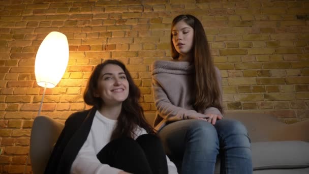 Retrato de chicas caucásicas jóvenes sentadas juntas y viendo películas con diversión positiva en un acogedor ambiente hogareño . — Vídeo de stock