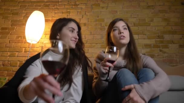 Junge kaukasische Mädchen sitzen mit Wein zusammen auf dem Fußboden und sehen Filme mit großer Aufmerksamkeit in gemütlicher Atmosphäre zu Hause. — Stockvideo