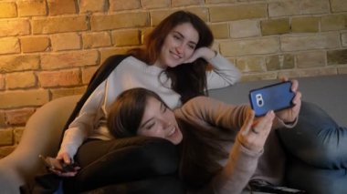Koltukta yalan ve selfie-fotoğrafları yapma genç beyaz kız portre rahat ev atmosferde smartphone kullanarak.