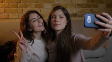 Katta oturan ve selfie-fotoğrafları yapma genç beyaz kızların yakın çekim shot rahat ev atmosferde smartphone kullanarak.